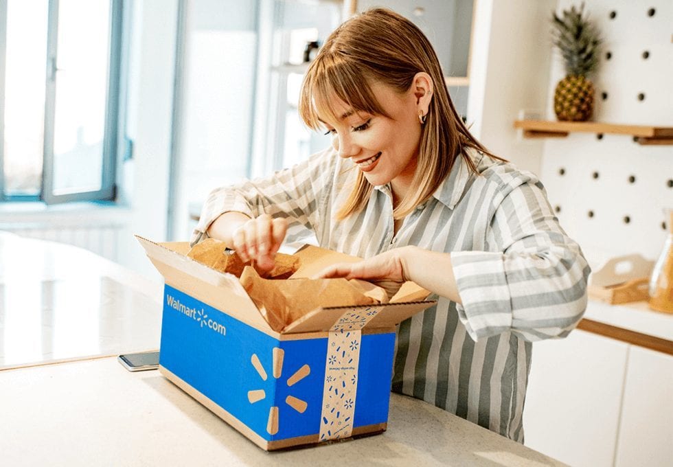 A woman opening a Walmart-branded shipping box at a kitchen counter